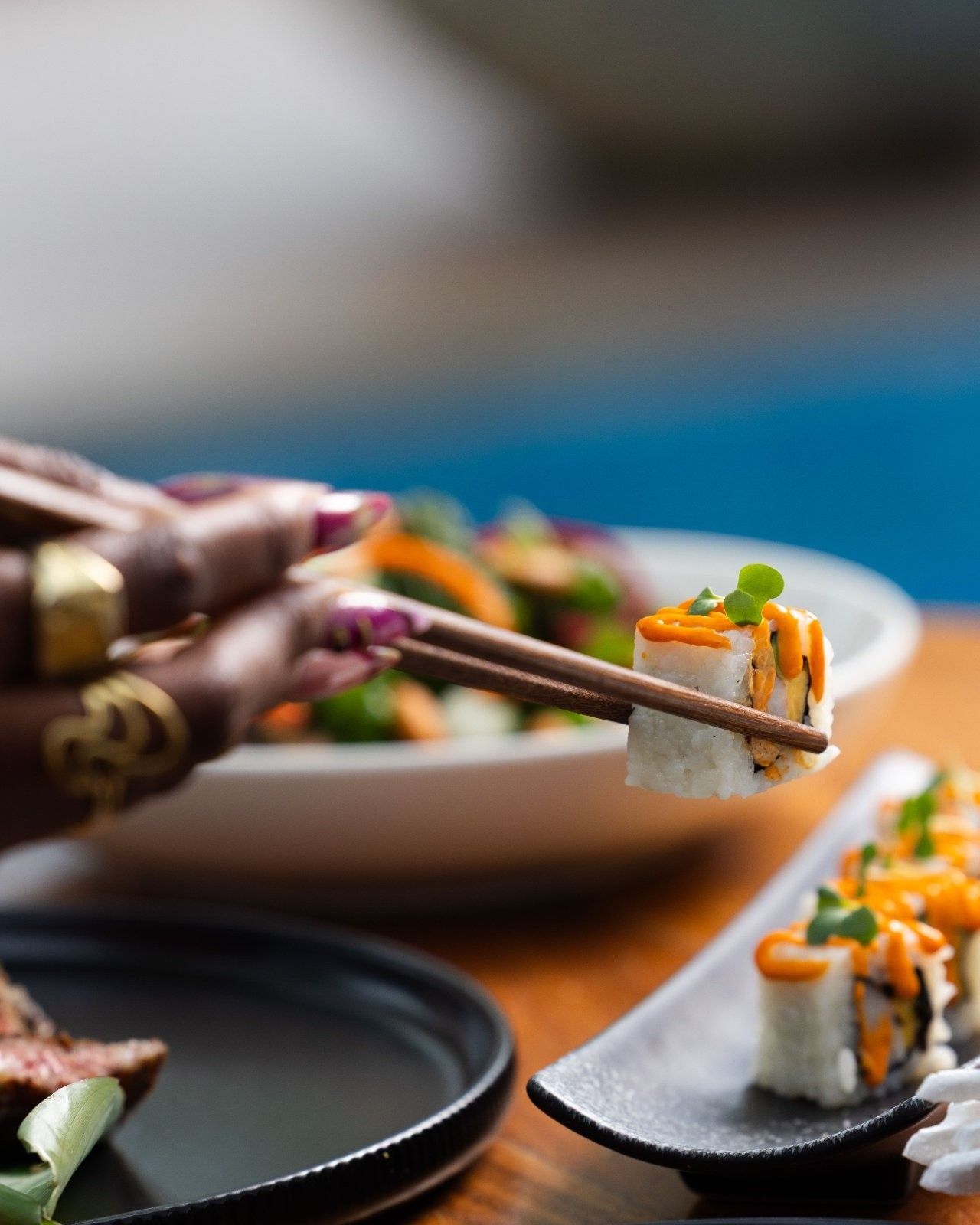 Sushi rolls topped with spicy mayo, held with chopsticks by the pool